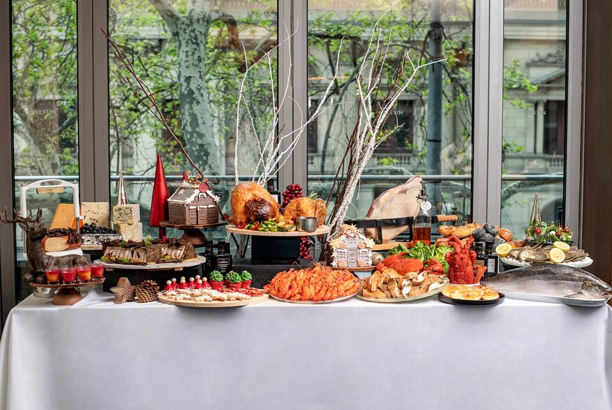 A table laden with a Christmas buffet in front of a window with trees outside.