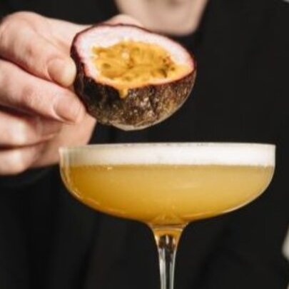 A bartender's hand squeezing a passionfruit over a Pornstar Martini.