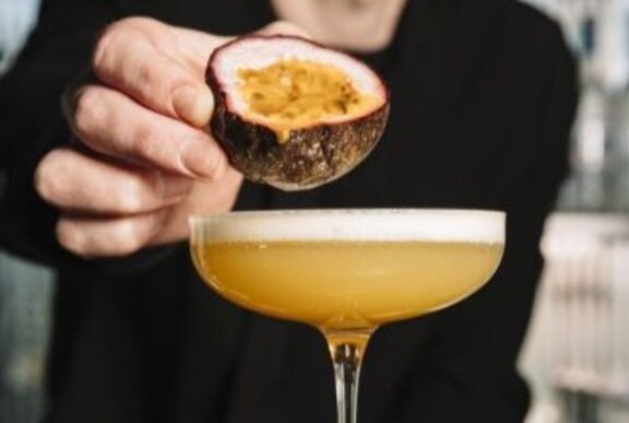 A bartender's hand squeezing a passionfruit over a Pornstar Martini.
