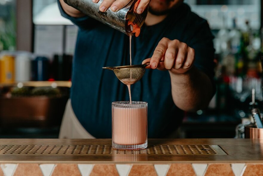 Bartender making a pink cocktail at a bar.