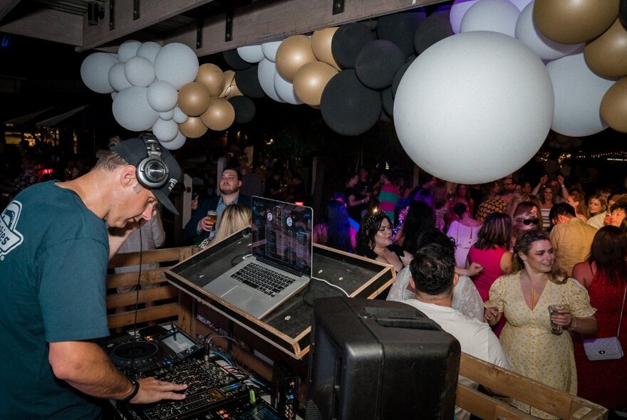 A DJ performing at a venue with many people dancing and bunches of balloons.