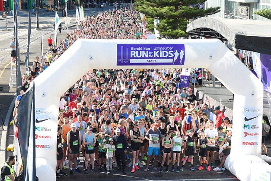 A very large crowd of participants in the Run for the Kids, waiting at the starting line behind an inflatable arch, on a road in Melbourne.