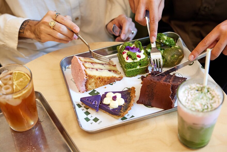 A silver tray of cakes next to two colourful drinks.
