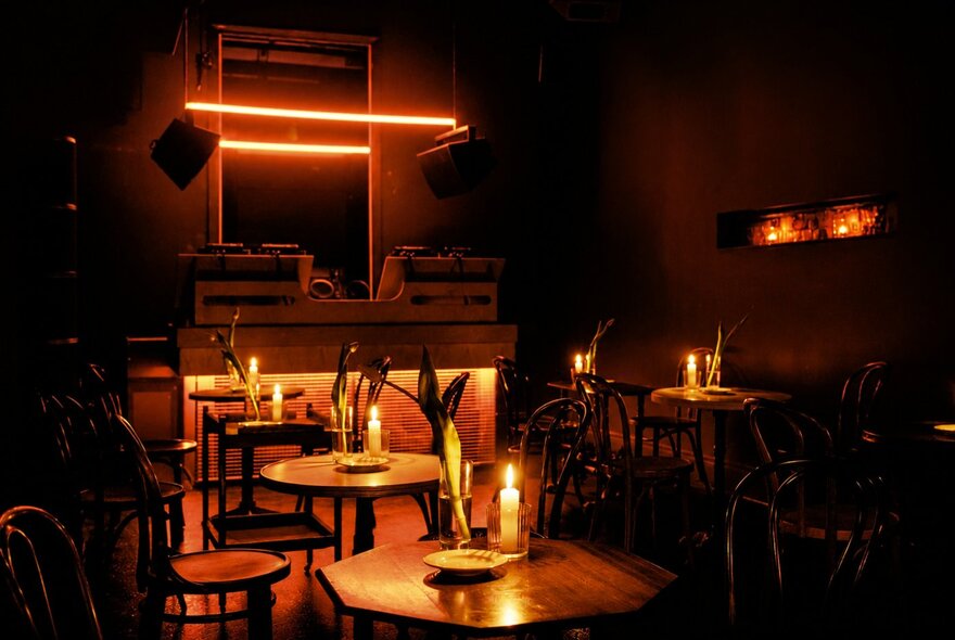 The glow of candles on small tables in a very dark bar. 