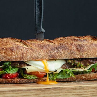Egg yolk pouring out of a long sub sandwich with cheese and salad.