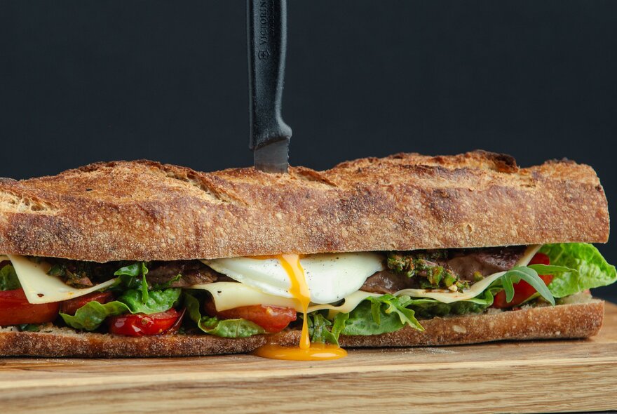 Egg yolk pouring out of a long sub sandwich with cheese and salad.