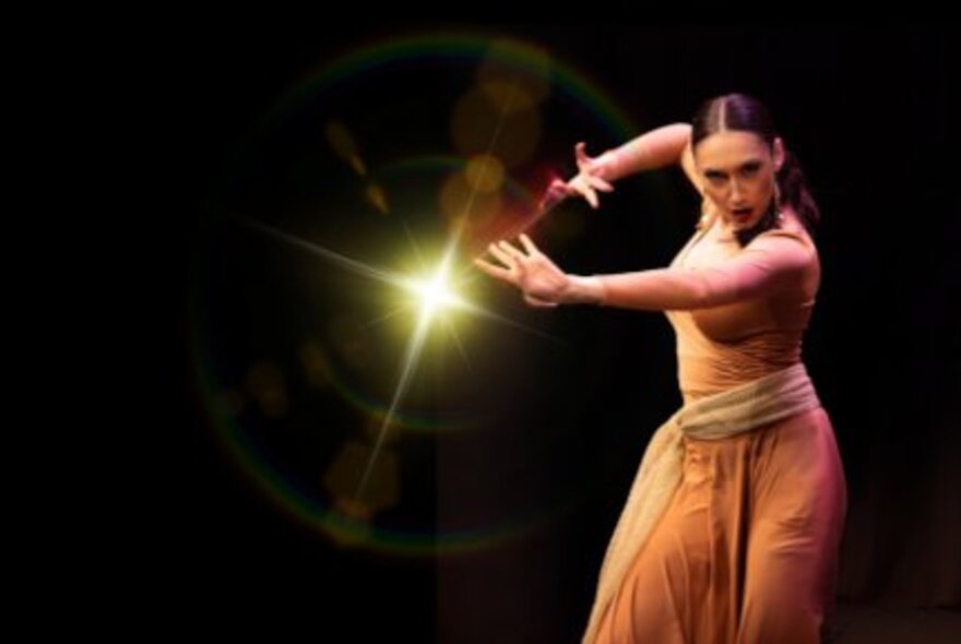 A flamenco dancer on a darkened stage, her arms stretched out in front of her, her gaze intense.