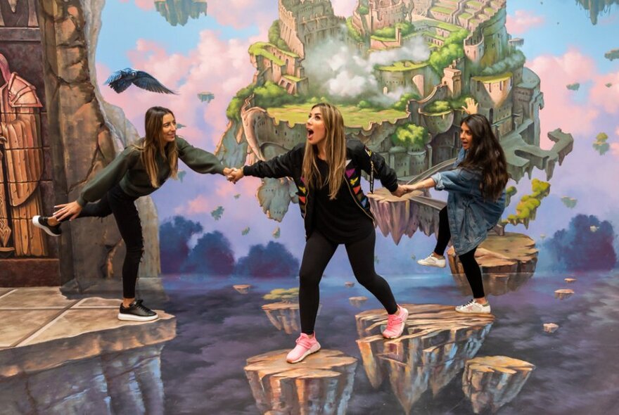 Three women joining hands and fooling around in a hand-painted interactive artwork of a fantasy landscape at ArtVo.