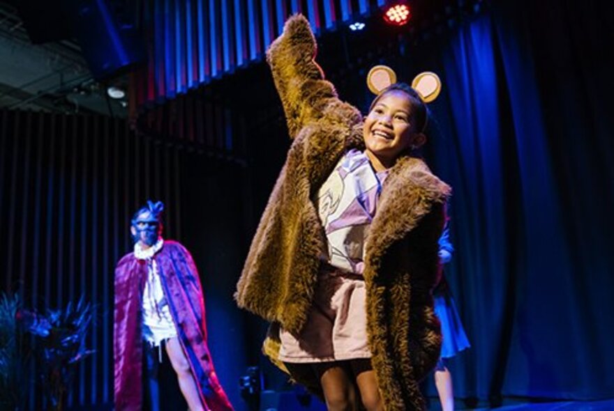 Child performing on stage wearing a rur coat and mouse ears.