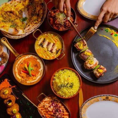Hands arranging food from an array of Indian dishes including saffron rice and curries.