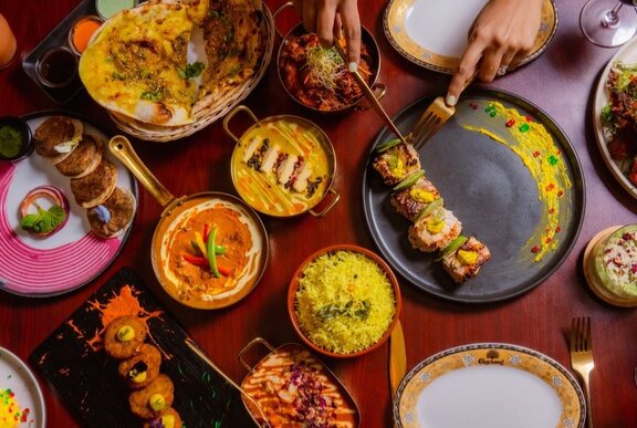 Hands arranging food from an array of Indian dishes including saffron rice and curries.