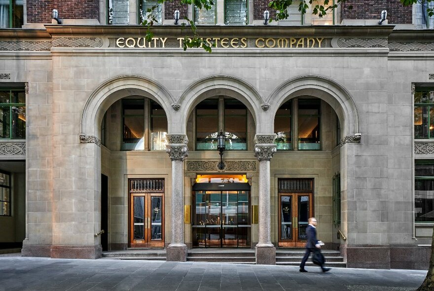 The exterior of Hilton Melbourne Little Queen Street showing it's three arches, a man walking past. 