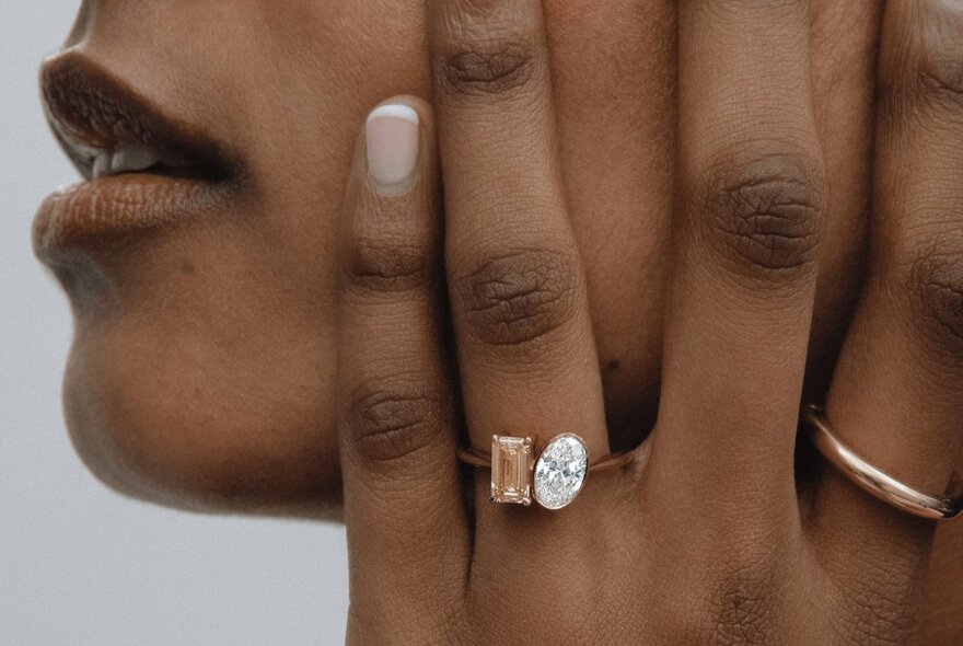 A close-up of a ring with two large diamonds and a gold hoop on a woman's hand as she holds it up to her face