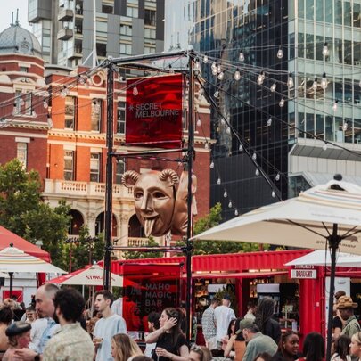 Exterior of Spiegel Haus with patrons mingling outside under umbrellas and festoon lights; city buildings in the background.