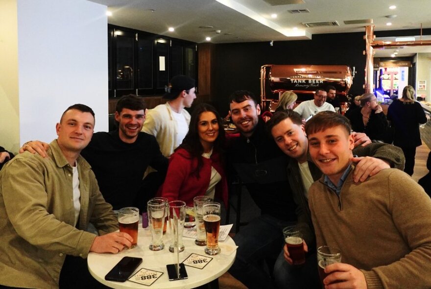 A group of people in a sports bar, seated at a table with glasses of beer.