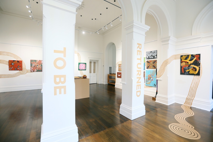 An arched gallery space with polished hardwood floors and First Nations artworks displayed on the walls.