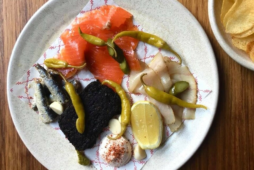 White dish with sardines, salmon and accompaniments.