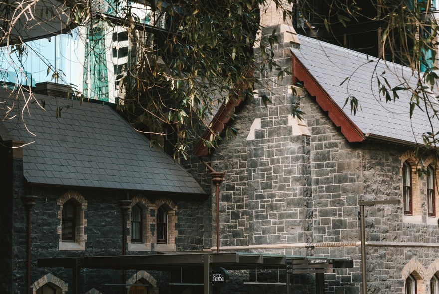 An old bluestone building with gumtrees around it. 