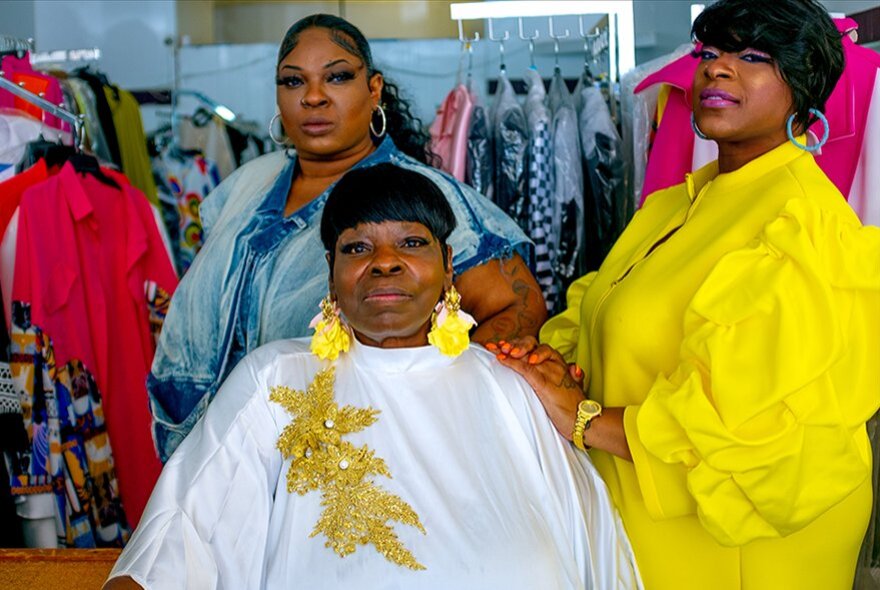 Black American women wearing bold white and colours, surrounded by racks of clothing.