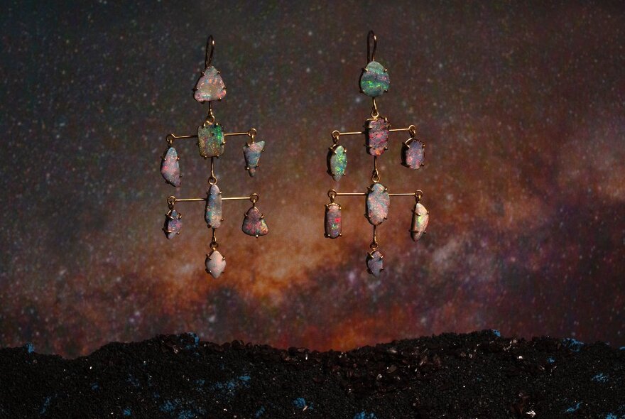 Dangling earrings featuring multiple small opals, set against a dark background.