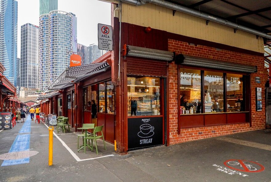 The red brick exterior of STREAT cafe at Queen Victoria Market, the Melbourne city skyscrapers visible down the laneway. 