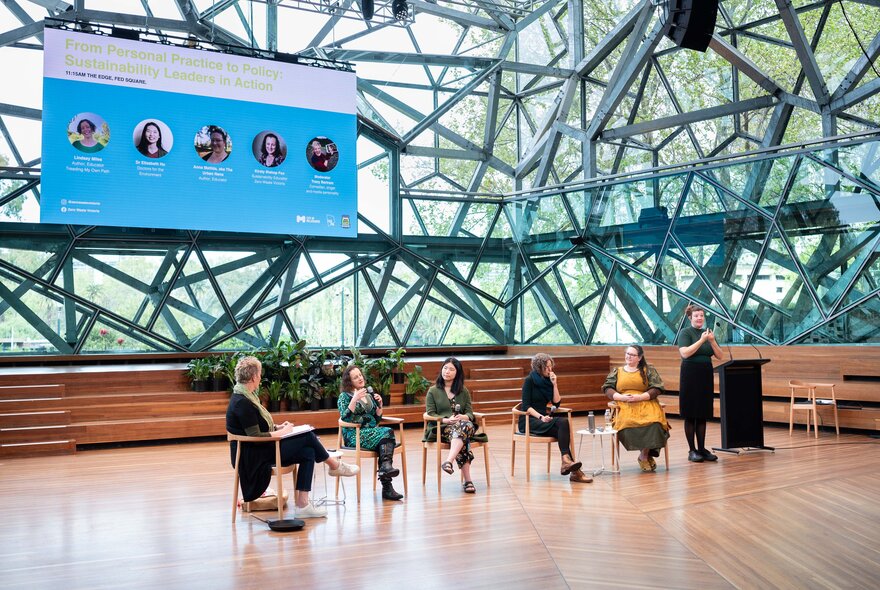Panellists seated on a stage in the Edge venue with large screen behind them.