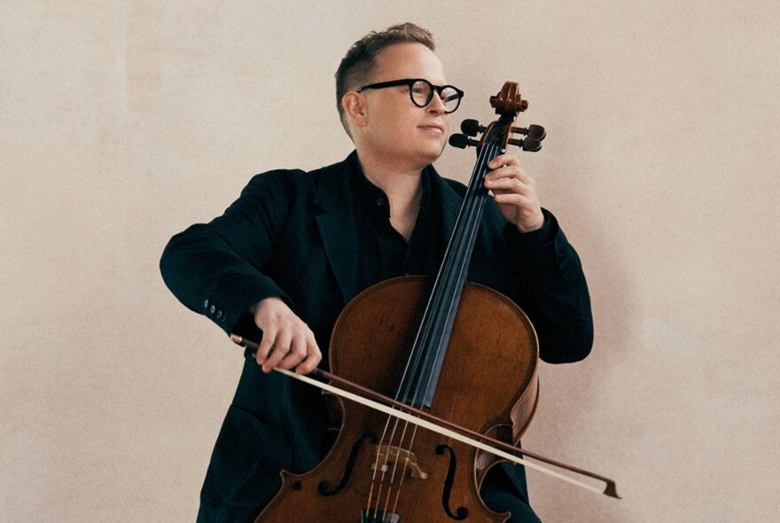 Classical musician playing a cello, wearing a dark coat and glasses.