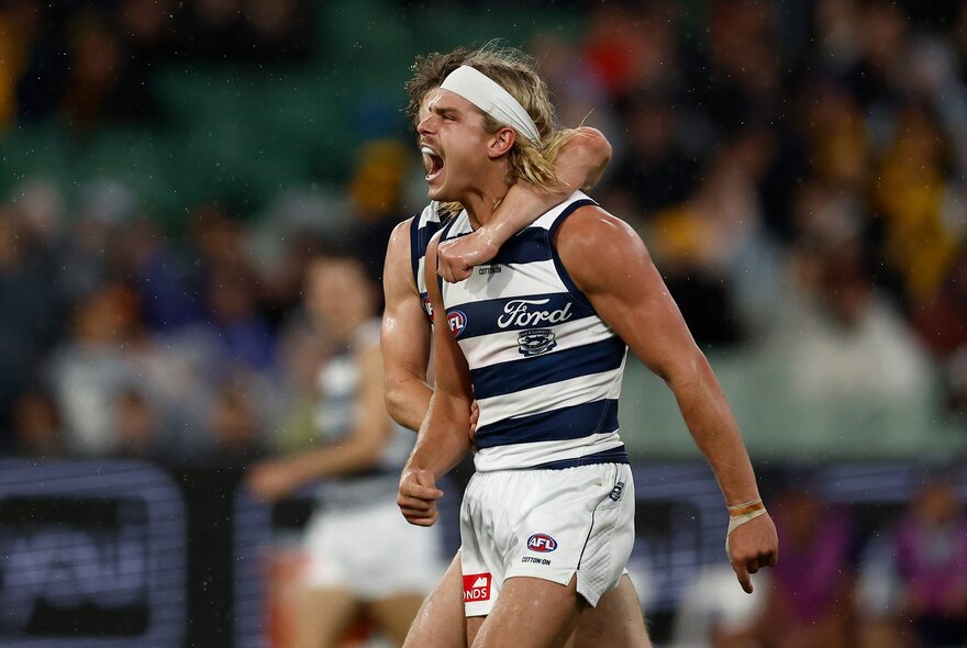 Two Geelong AFL football players in a clinch during a match.