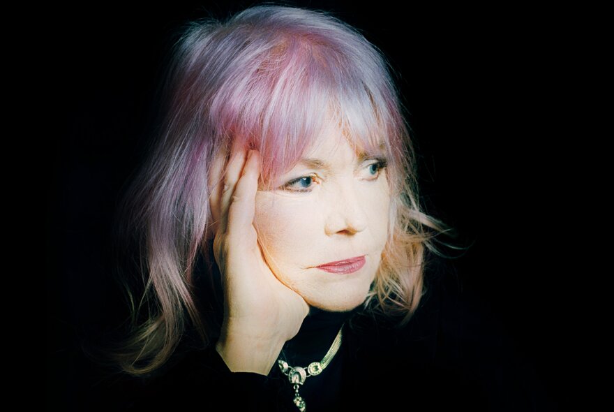 Singer Margie Lou Dyer looking to one side, her head is resting on her hand, she has light coloured hair framing her face.