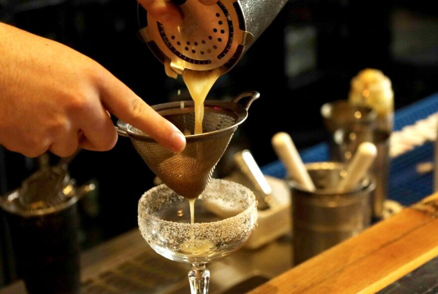 A bartender pouring a drink into a glass from a cocktail shaker.