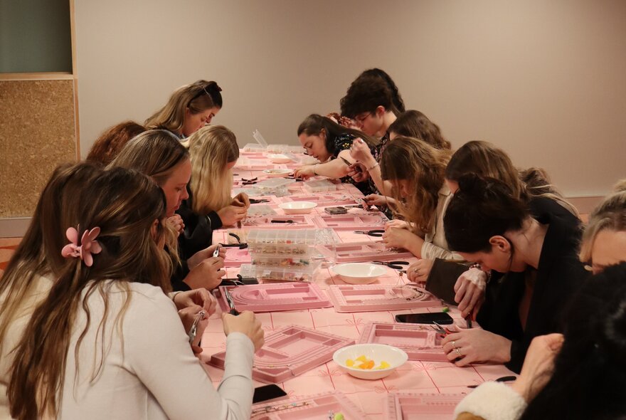 A workshop with women at a table with a pink tablecloth working on projects. 