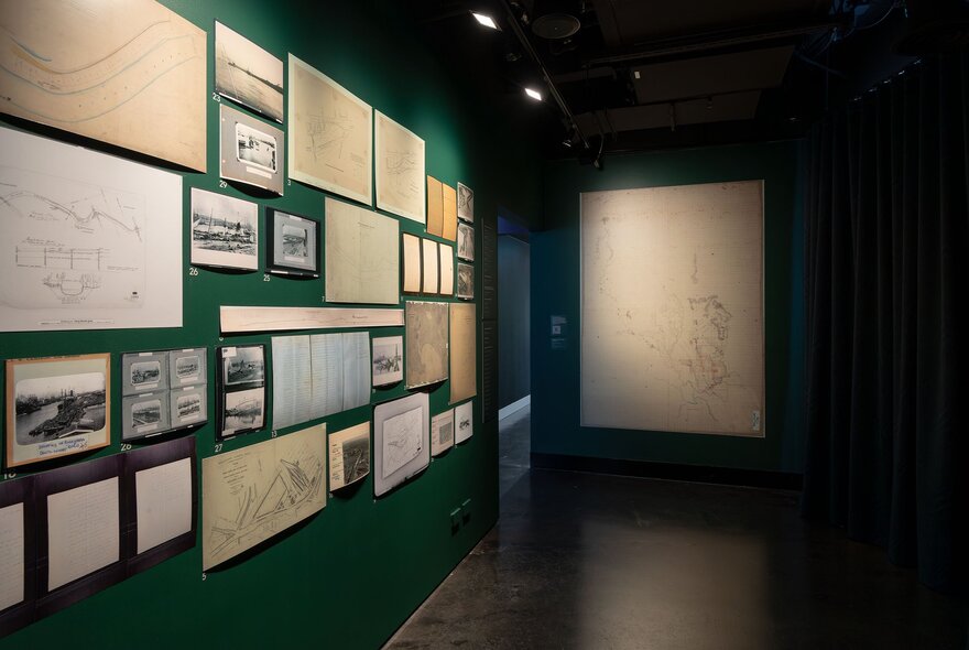 Inside a darkened gallery space with many small pictures and works on the wall.