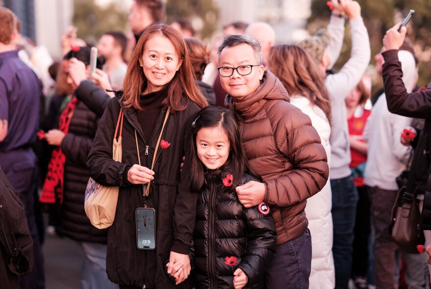A family posing in winter jackets with red poppies pinned to their fronts, a crowd of people in the background.