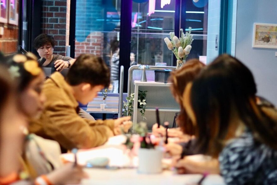 A room with a long table where people appear to all be holding pencils and working on a task. 