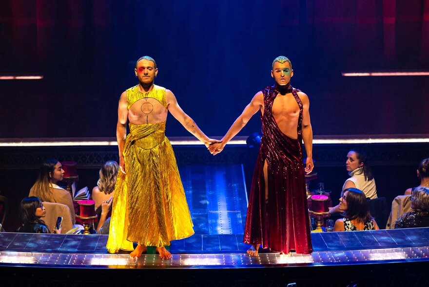 Male models wearing skirts, holding hands on a runway.