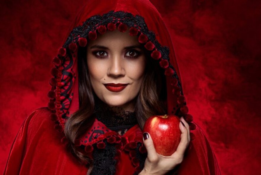 Woman wearing a red cloak, holding a red apple.