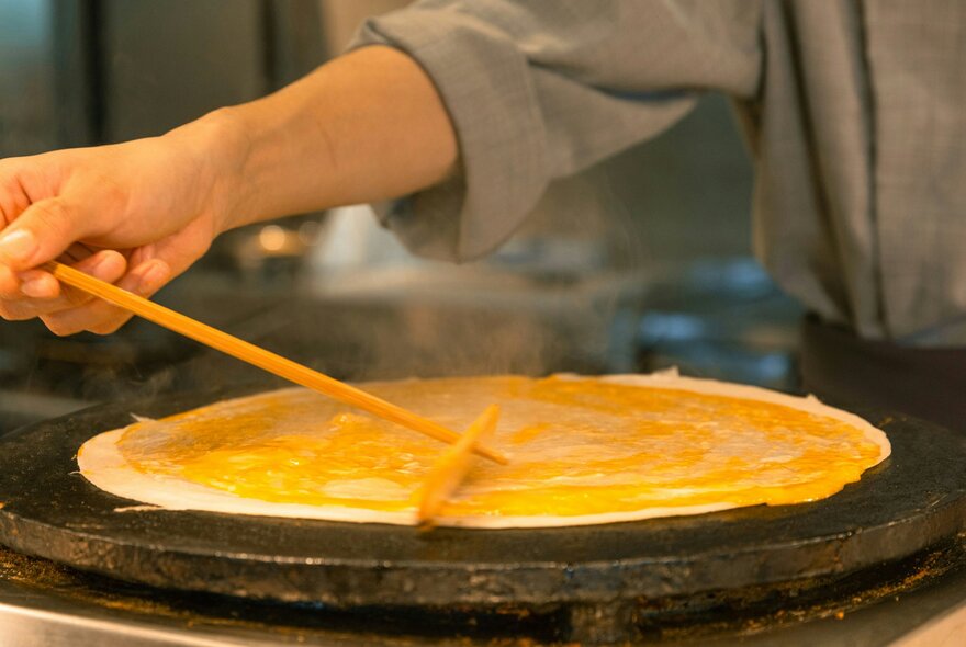 A person is making a crepe on a hot plate