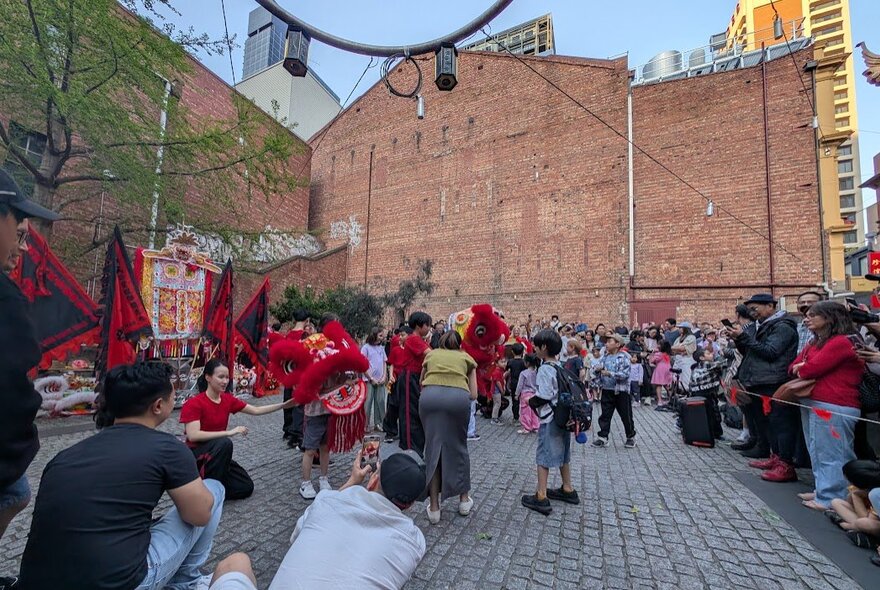 Outdoors at a Chinese festival with people wearing dragon heads and people looking on.