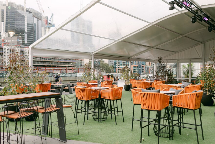 Bar seats on an astroturf deck with city buildings and cranes in the background.