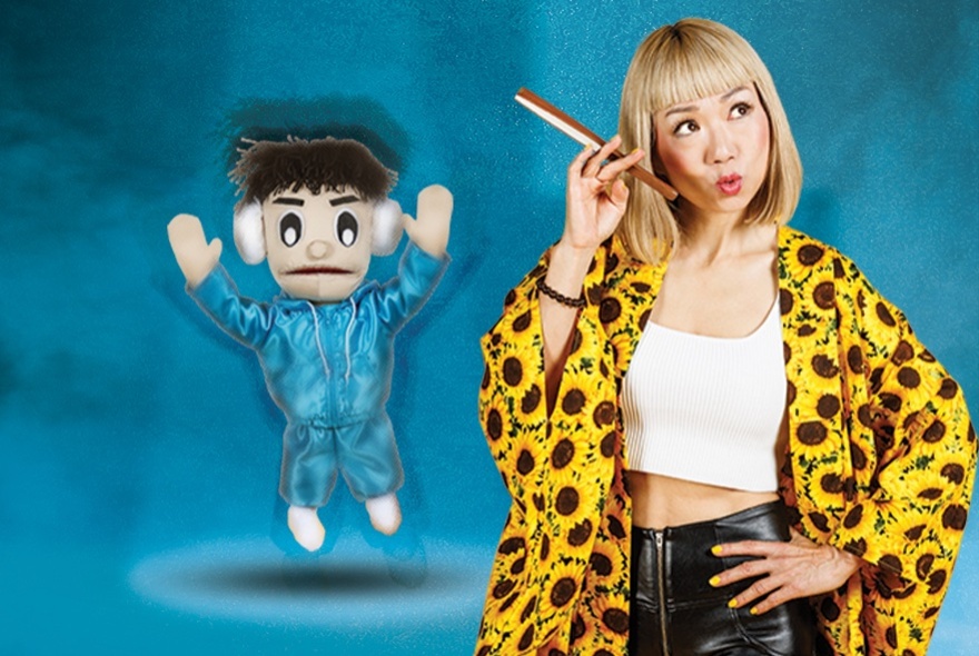 Performer Showko in a top with sunflowers on it and listening to a phone with a little toy man in a blue tracksuit next to her. 