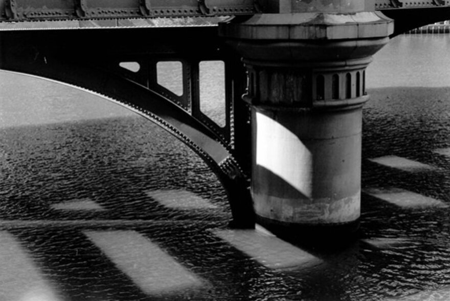 A black and white detail of a bridge pylon showing metal and stone construction. 