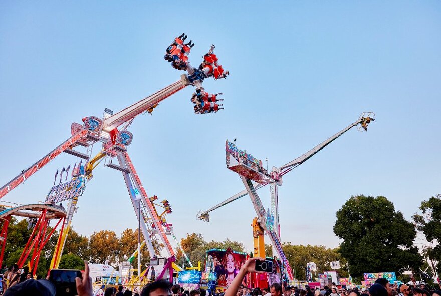 People on carnival rides being swung around in the air with crowds gathered underneath.