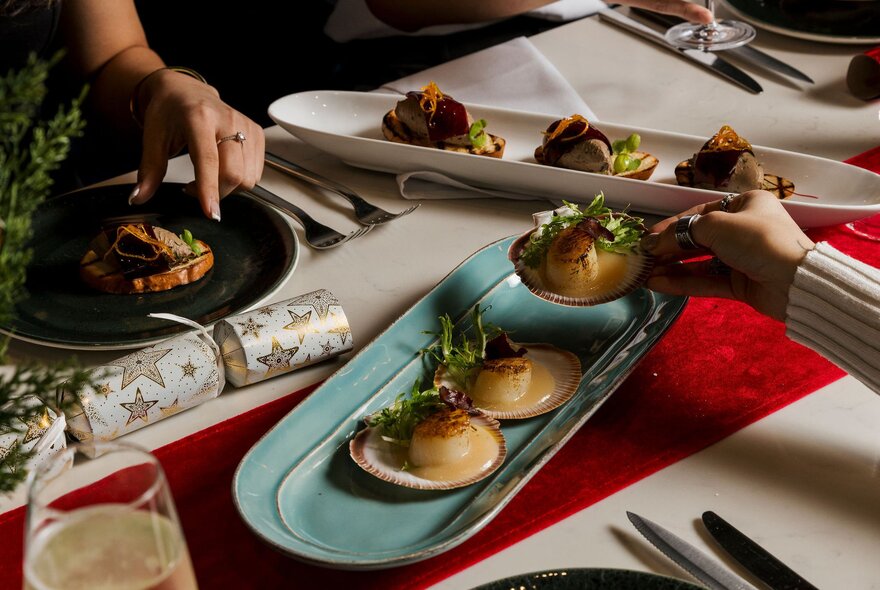 A tray of scallops on a table, a person reaching for one.