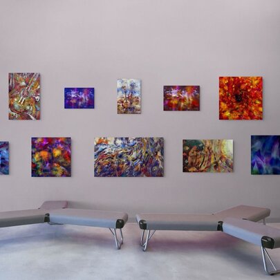 A gallery space with many colourful smaller paintings on the wall and two tri-shaped seats close to each other. 