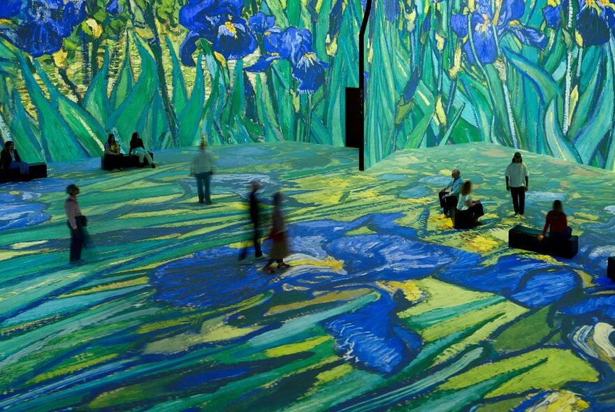 People walking around a very large exhibition space with Vincent van Gogh's paintings of blue iris flowers digitally projected on all the wall and floor spaces.