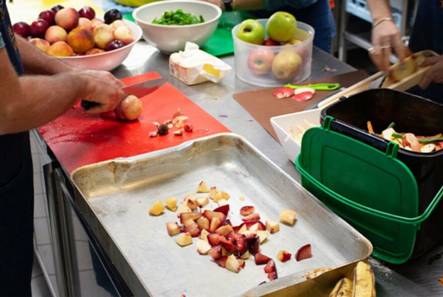 Hands preparing a tray of chopped fruit.