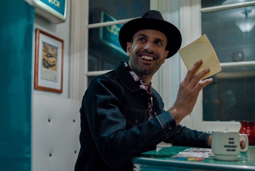 Man wearing a hat, holding a piece of paper above a cup at a table.