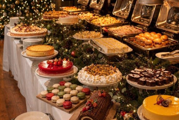 A generous high tea spread with full platters of savoury and sweet treats arranged on a long buffet table.