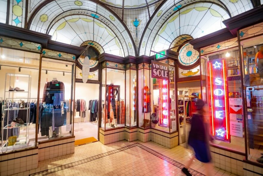 A blurred shopping walking past shops with stained glass arched windows and neon lights.