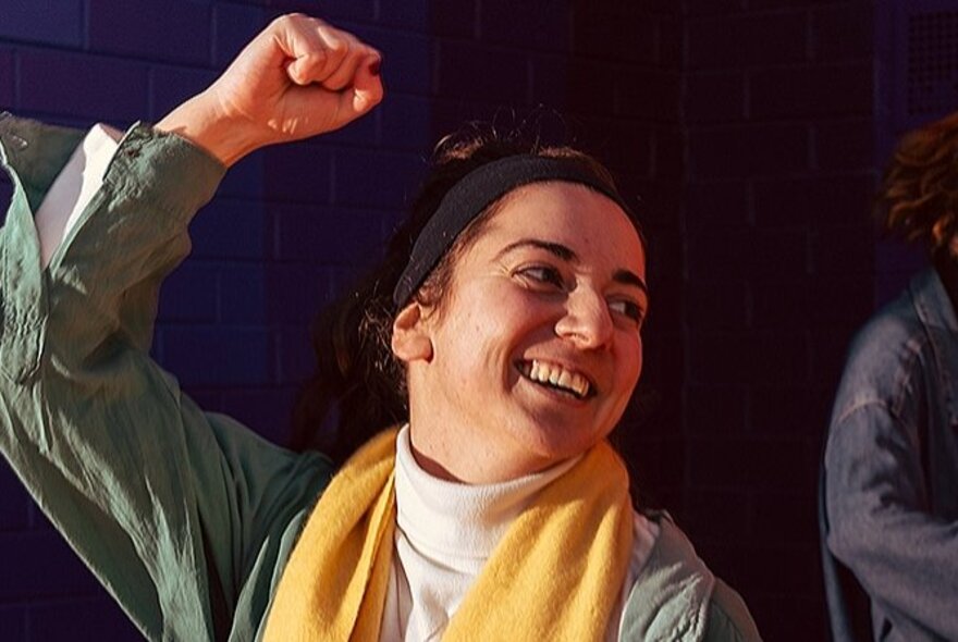 A smiling woman looking off to the side, with her right arm in the air, dancing.